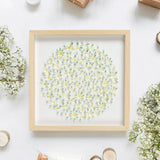 Flatlay view of framed daisy paper artwork surrounded by delicate white flowers