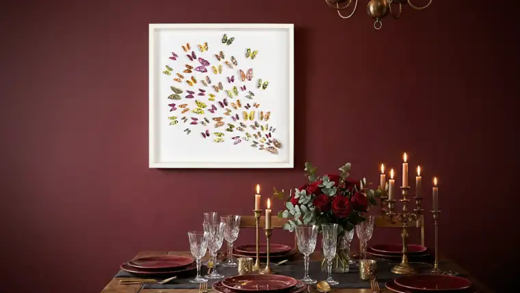 Framed 3D watercolor butterfly paper artwork displayed on a burgundy wall above an elegant dining table with candles and flowers.