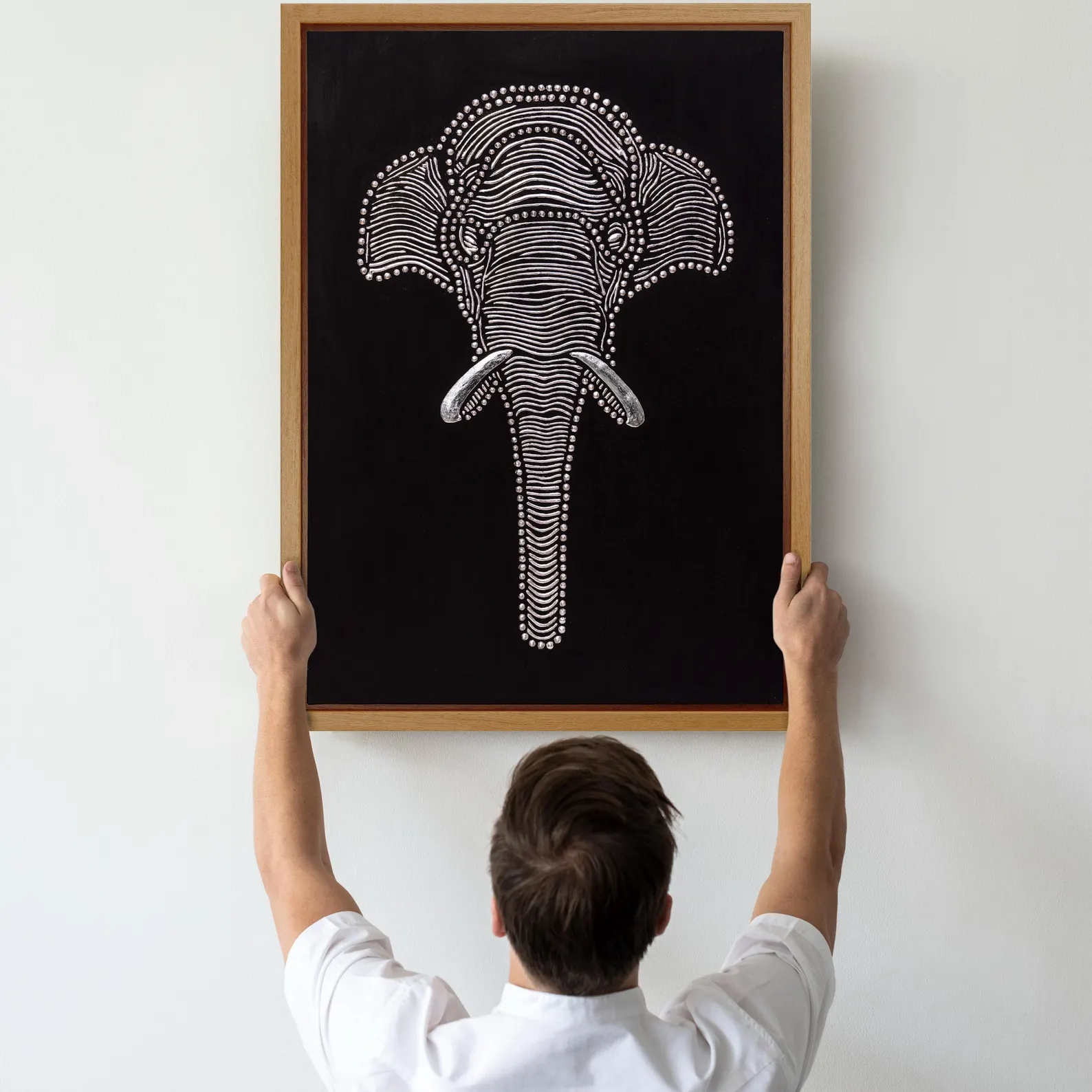 Scale view of textured elephant wall art being placed on a wall, showing the framed black relief canvas size.